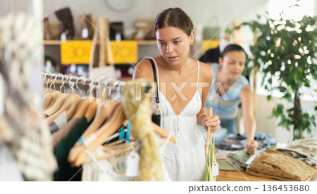Positive joyful woman looking for fashionable clothes in clothing boutique Positive joyful woman looking for fashionable clothes in clothing boutique 136453680