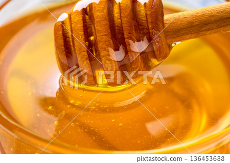 Fresh honey drips from a wooden honey spoon on a plate close-up . honey dipper being submerged into a glass jar. 136453688