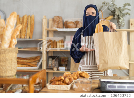 Muslim European woman in niqab bakery worker sells baguettes, stand at counter and wait for visitors Muslim European woman in niqab bakery worker sells baguettes, stand at counter and wait for visitors 136453733