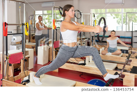 Sportive young girl training her arms and legs on reformer device Sportive young girl training her arms and legs on reformer device 136453754