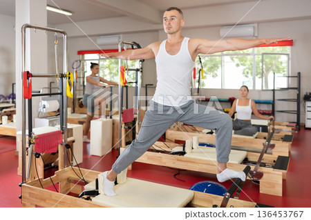 Sportive young guy training her arms and legs on reformer device 136453767