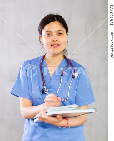Female doctor in blue uniform filling out medical form 136453771