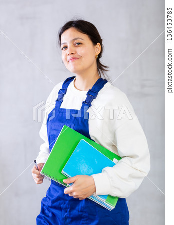 Positive female builder in blue jumpsuit holding engineering documentation Positive female builder in blue jumpsuit holding engineering documentation 136453785