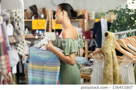 Positive joyful woman looking for fashionable clothes in clothing boutique 136453807