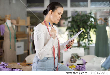 Puzzled dressmaker with documents in her hands Puzzled dressmaker with documents in her hands 136453815