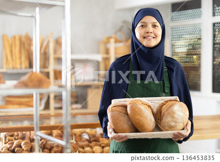 Asian Muslim woman bakery worker sells bread, stand at counter and wait for visitors Asian Muslim woman bakery worker sells bread, stand at counter and wait for visitors 136453835