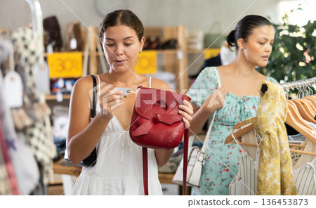 Happy young woman choosing handbag in clothing store Happy young woman choosing handbag in clothing store 136453873