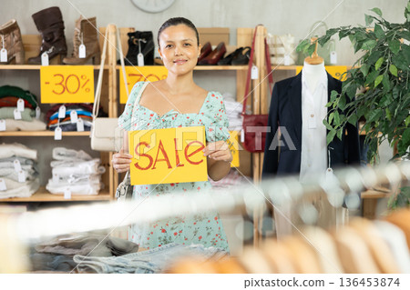 Smiling asian woman holding a sign saying Sale in the interior of fashion store Smiling asian woman holding a sign saying Sale in the interior of fashion store 136453874