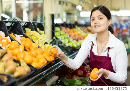 Asian female seller in apron chooses ripe mandarin 136453875