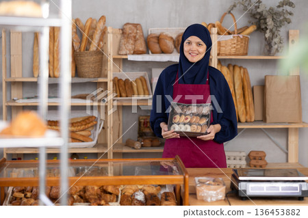 Middle-aged Muslim saleswoman holds cookie box in bakery Middle-aged Muslim saleswoman holds cookie box in bakery 136453882