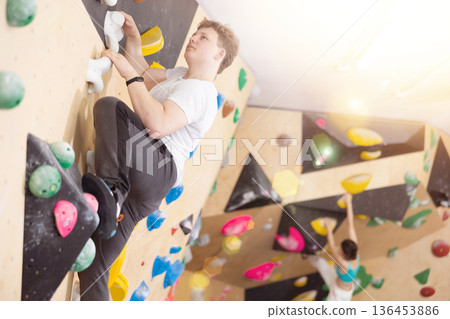 Teenage boy climbs steep artificial wall in sports complex and trains endurance Teenage boy climbs steep artificial wall in sports complex and trains endurance 136453886