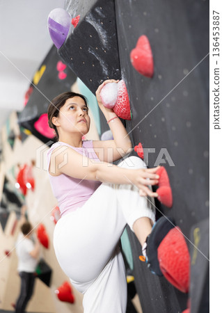 Sporty woman climbing on bouldering wall demonstrating physical strength, technical skill, and determination 136453887