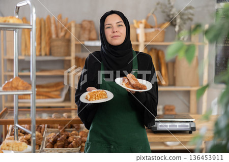 European Muslim girl employee of bakery stands with sandwiches in disposable plates European Muslim girl employee of bakery stands with sandwiches in disposable plates 136453911