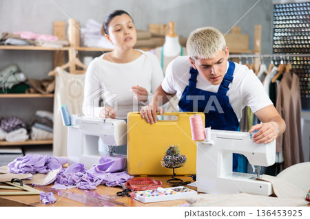 Professional young repairman master repairing sewing machine in sewing workshop, excited asian woman seamstress asking questions Professional young repairman master repairing sewing machine in sewing workshop, excited asian woman seamstress asking questions 136453925