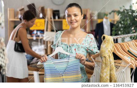 Positive young Asian woman choosing something for summer in clothing store 136453927