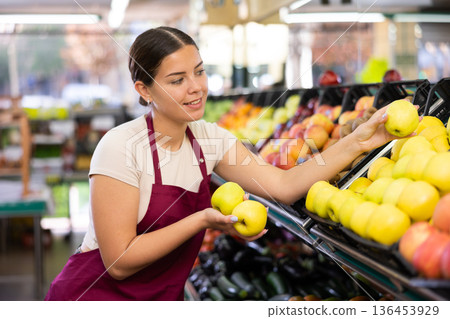 Female seller in apron chooses juicy apple Female seller in apron chooses juicy apple 136453929