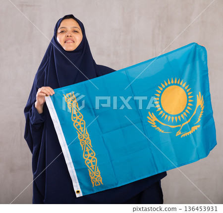 Young Muslim woman in blue hijab holds unfurled flag of Kazakhstan Young Muslim woman in blue hijab holds unfurled flag of Kazakhstan 136453931