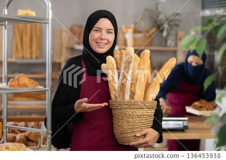 Portrait of girl seller of oriental bakery in traditional Muslim clothes with of baguettes Portrait of girl seller of oriental bakery in traditional Muslim clothes with of baguettes 136453938