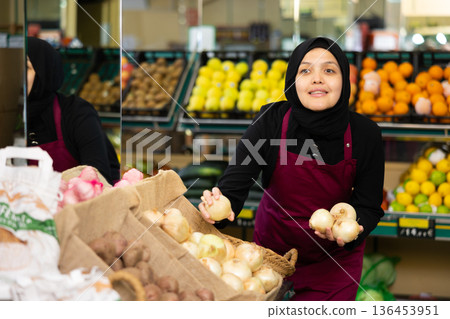 Muslim female seller in apron chooses quality onion 136453951