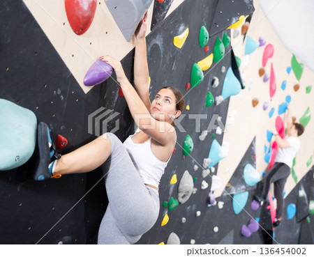 Young female alpinist practicing indoor a rock-climbing on a artificial boulder without safety belts 136454002