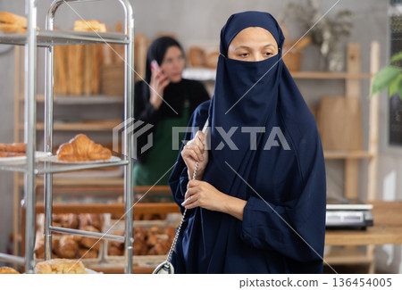 Muslim woman in niqab shopping for baked goods in bakery 136454005