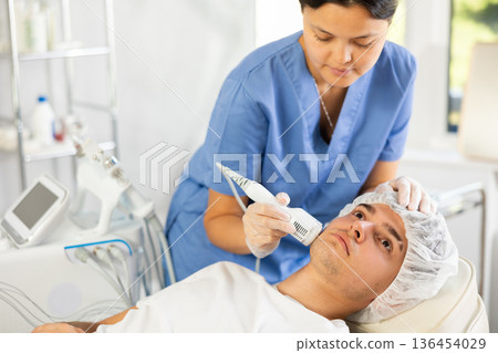 Young woman cosmetologist doing whitening procedure to young man 136454029