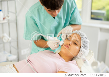Young male cosmetologist doing ultrasound procedure to young woman Young male cosmetologist doing ultrasound procedure to young woman 136454032