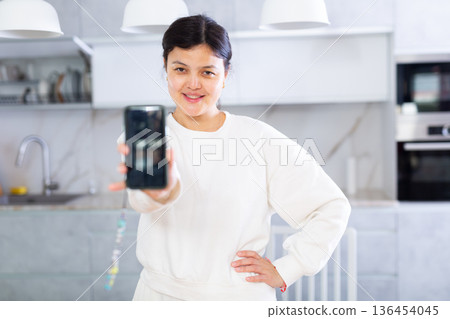 Young woman showing smartphone with blank screen in office kitchen Young woman showing smartphone with blank screen in office kitchen 136454045