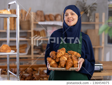Asian Muslim woman bakery worker sells croissants, stand at counter and wait for visitors Asian Muslim woman bakery worker sells croissants, stand at counter and wait for visitors 136454075