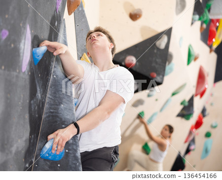 Teenage boy climbs steep artificial wall in sports complex and trains endurance Teenage boy climbs steep artificial wall in sports complex and trains endurance 136454166