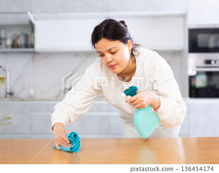 Positive young woman cleaning kitchen table at home 136454174