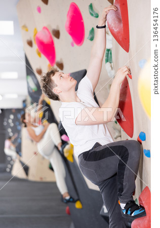 Teenage boy climbs steep artificial wall in sports complex and trains endurance Teenage boy climbs steep artificial wall in sports complex and trains endurance 136454176
