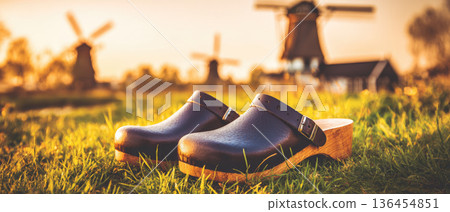 Dutch wooden clogs rest on green grass with windmills in background at sunset creating peaceful rural scene with traditional footwear and warm sunlight Dutch wooden clogs rest on green grass with windmills in background at sunset creating peaceful rural scene with traditional footwear and warm sunlight 136454851