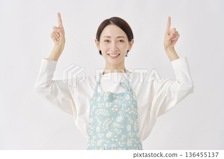 Woman wearing an apron pointing up, white background 136455137