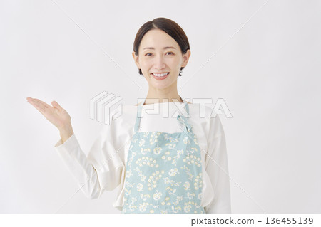 一位身穿圍裙的女子，在白色背景下用手掌指向左側。 136455139