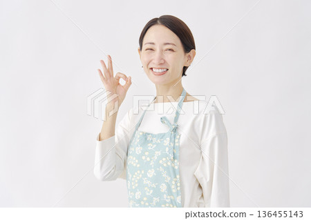 一位女士穿著圍裙，舉著「OK」手勢，白色背景 136455143