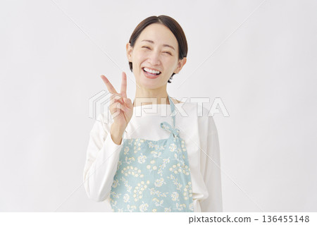 Woman wearing an apron making a peace sign on a white background Woman wearing an apron making a peace sign on a white background 136455148