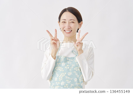 Woman wearing an apron making a peace sign on a white background Woman wearing an apron making a peace sign on a white background 136455149