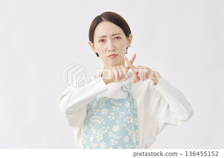 Woman wearing an apron making a cross gesture on a white background 136455152