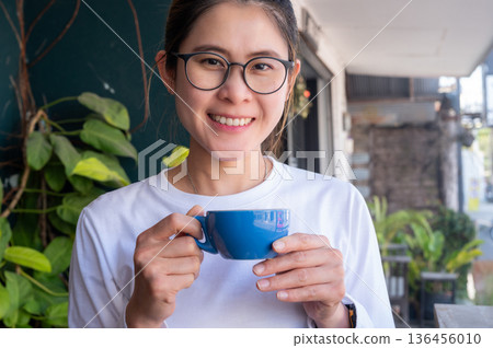 Asian woman holding a cup of hot Cappuccino coffee before drinking. The taste of cappuccinos can be described as creamy, smooth, and balanced. 136456010