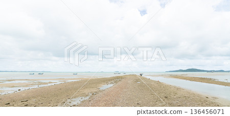 Wide shot of a coastal sandbar during low tide with traditional fishing boats in the distance. Minimalist seascape featuring a bright cloudy sky and calm ocean water at a tropical beach. Wide shot of a coastal sandbar during low tide with traditional fishing boats in the distance. Minimalist seascape featuring a bright cloudy sky and calm ocean water at a tropical beach. 136456071