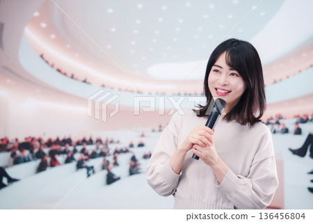 一位女士在眾多觀眾面前對著麥克風講話。 一位女士在眾多觀眾面前對著麥克風講話。 136456804