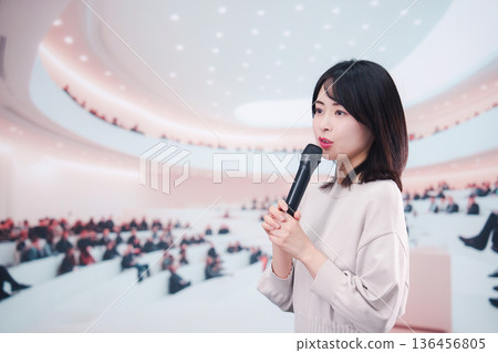 一位女士在眾多觀眾面前對著麥克風講話。 一位女士在眾多觀眾面前對著麥克風講話。 136456805