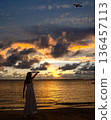 Image of a woman in a dress pointing at an airplane at sunset on a tropical beach 136457113