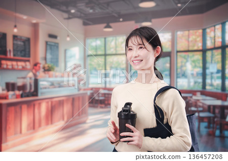 一位年輕女子拿著自己的杯子走進咖啡館。 136457208
