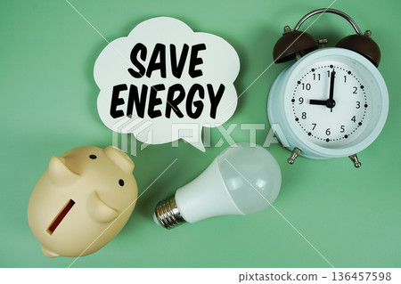 Save Energy with light bulb, piggy bank and alarm clock on green background 136457598