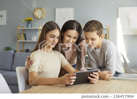 Young mother sitting with children using tablet together browsing internet at home. 136457904