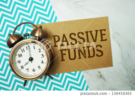 Passive Funds text written on paper card with alarm clock on marble background 136458365
