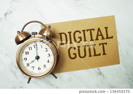 Digital Guilt text written on paper card with alarm clock on marble background Digital Guilt text written on paper card with alarm clock on marble background 136458370