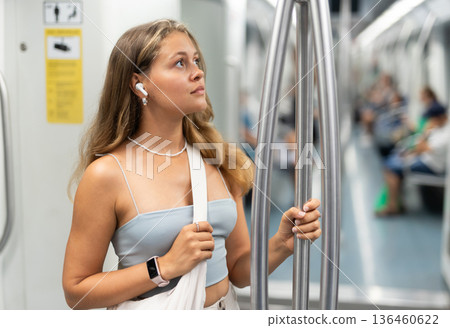 Young woman with headphones standing in metro car Young woman with headphones standing in metro car 136460622
